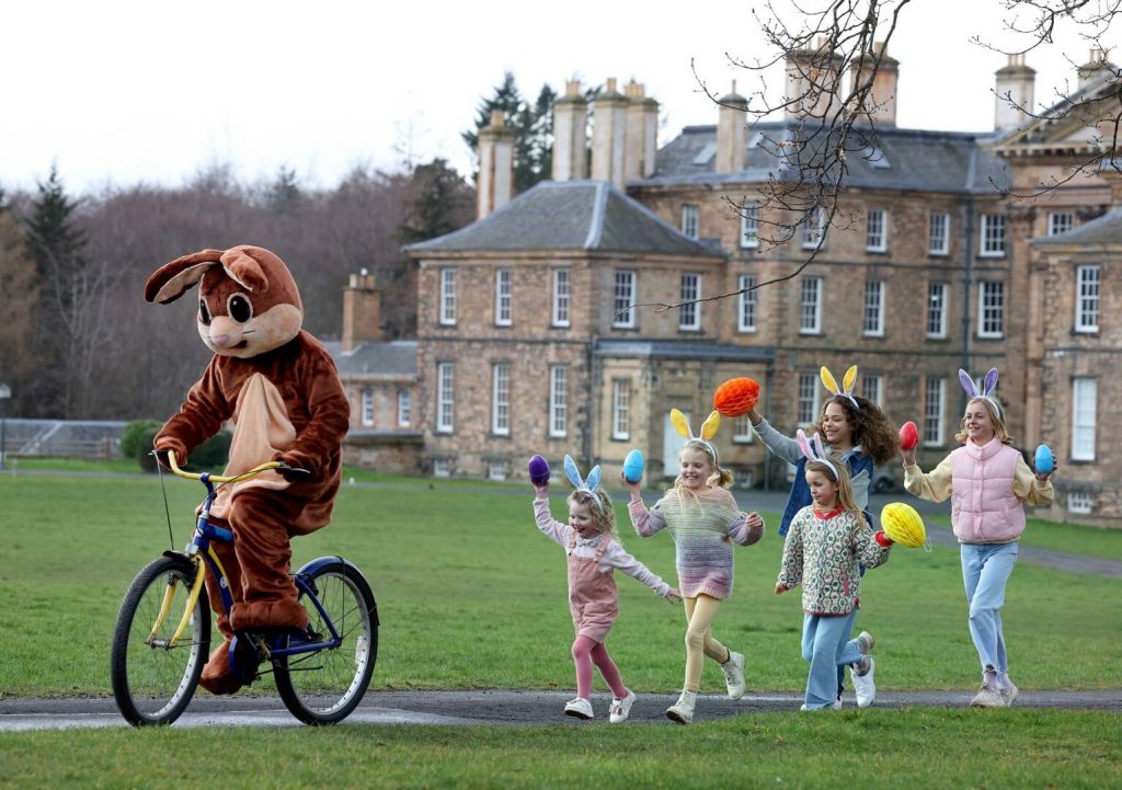 Easter Bunny cycling in front of Dalkeith Palace with children running behind him