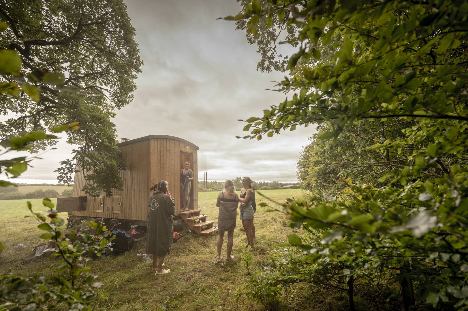 A group of friends cooling down and chatting outside the sauna beside the Ale Water, before going back in to the steam., Cedar Hus and Phil Wilkinson Photography