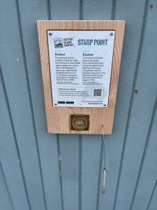 Photograph of a Scottish Islands Passport stamping point showing an information board and a brass rubbing plate mounted on a wooden back