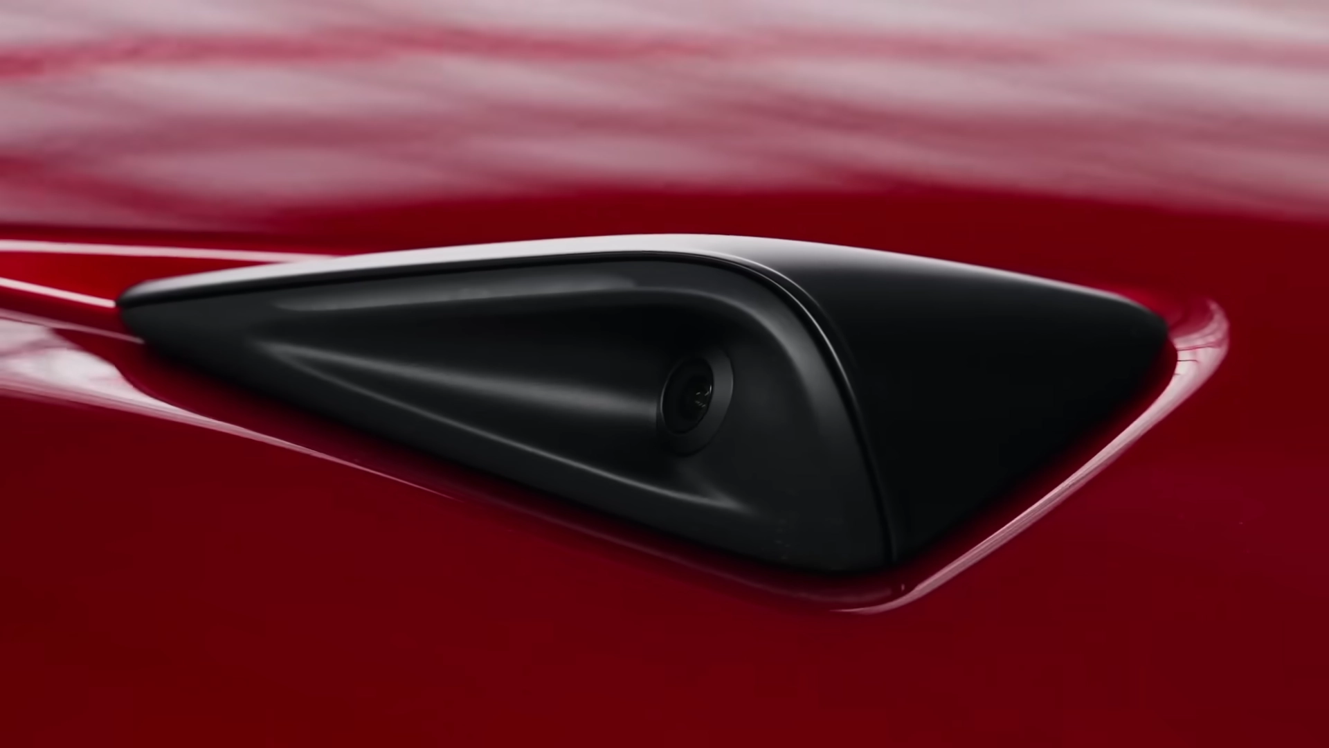 A close-up view of the front bumper camera housing on a red Tesla, highlighting the hardware feature that is missing from current Model 3 production units.
