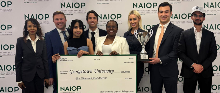 Group of eight individuals pose in front of a NAIOP backdrop while holding a large ceremonial check and a trophy.