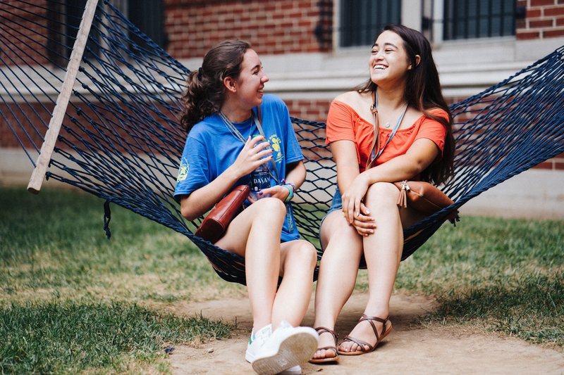 Two female students sitting on hammock talking on Georgetown campus.