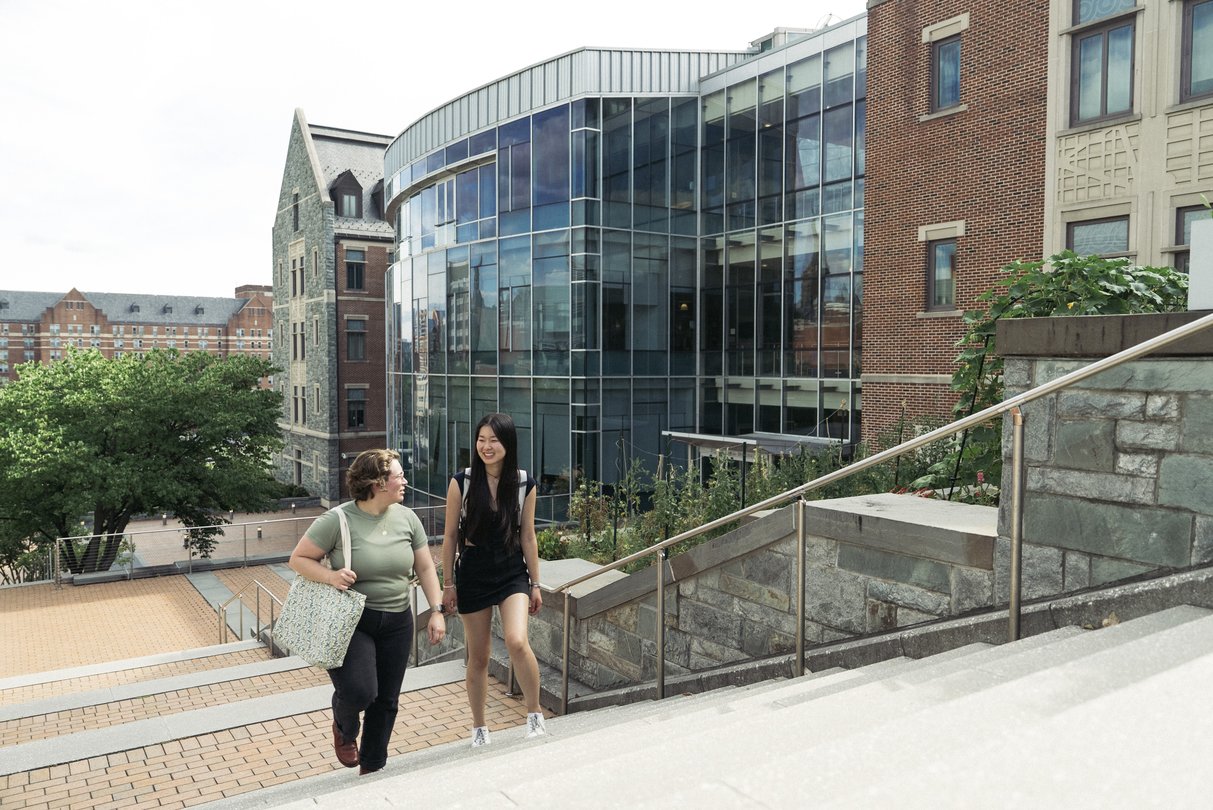 Georgetown University students walking and talking near a modern glass academic building on campus.