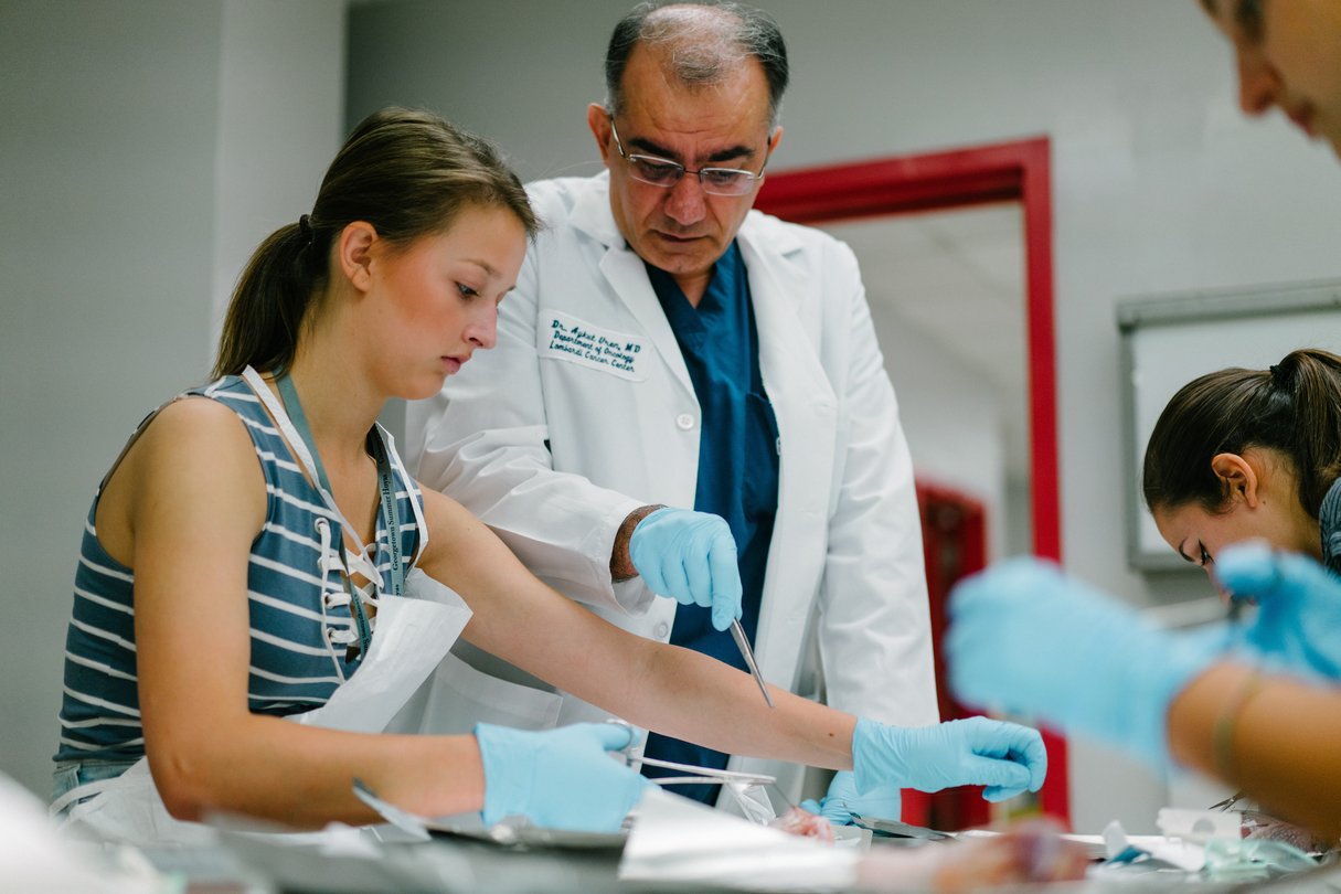 Medical professional standing next to student, instructing how to make a suture