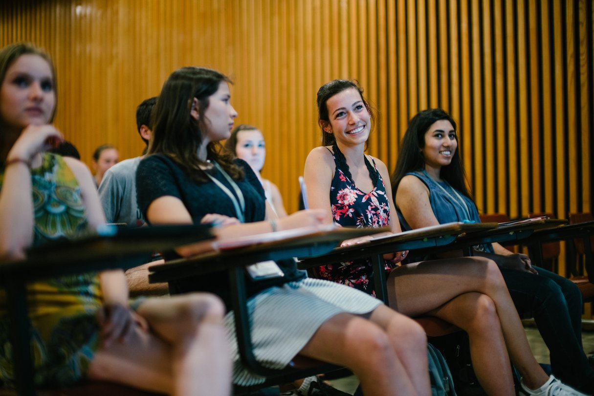 Students sitting in desks listening in lecture hall.