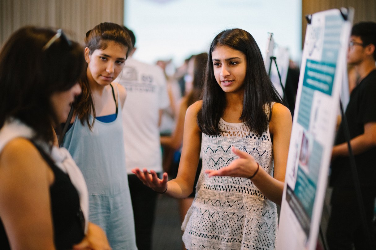 Female student presenting a poster board with images and information to audience members.