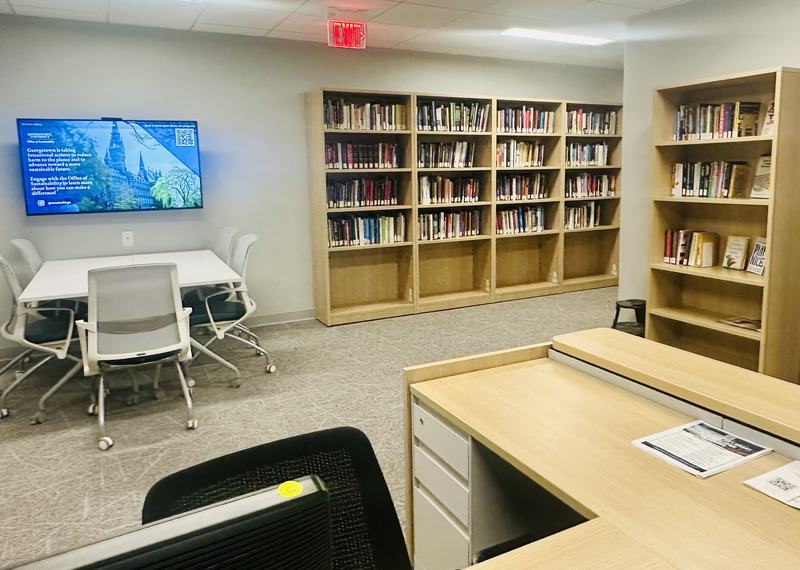 A library with bookshelves full of books, wooden reception desk, and a TV mounted on the wall above a meeting space.