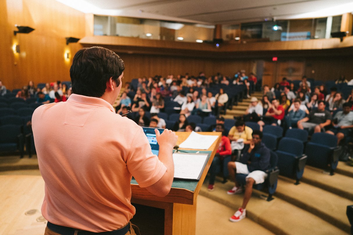 Over the shoulder shot of professor lecturing  at podium to a lecture hall.