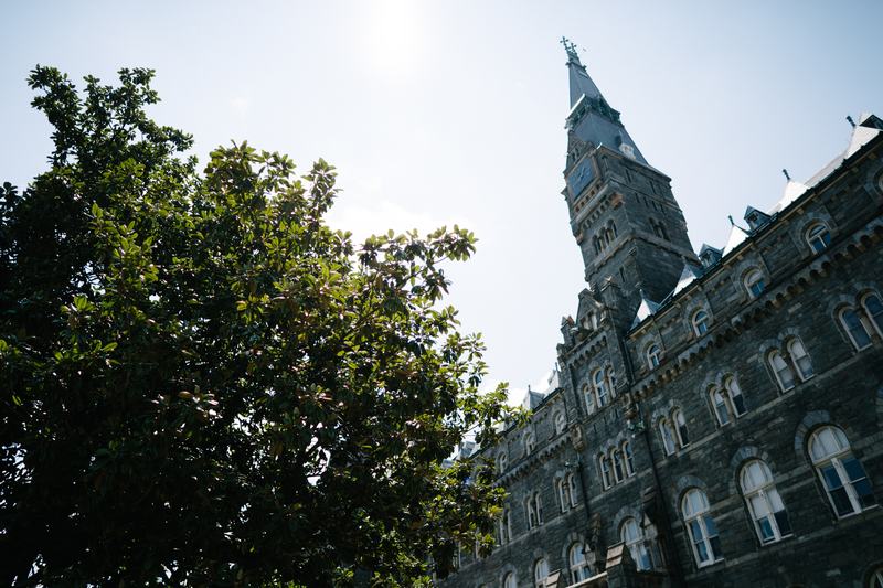Georgetown University’s historic Healy Hall clock tower framed by green trees under a clear blue sky.