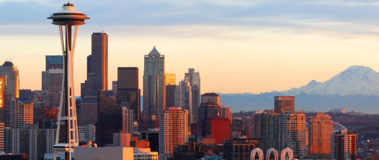 Seattle skyline at sunset featuring the Space Needle in the foreground, downtown skyscrapers, and Mount Rainier visible in the distance.