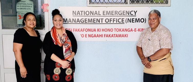 Three people stand in front of a sign for the National Emergency Management Office (NEMO), posing for a photo outside the office building.