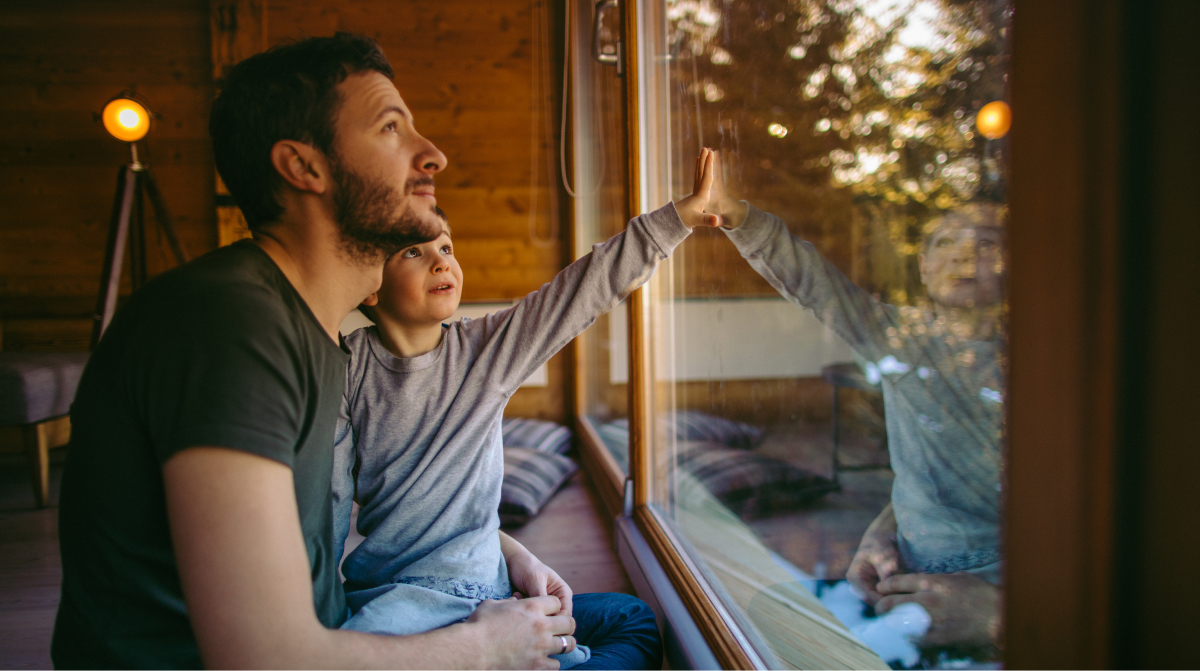 A father and son looking up out a window. The child is touching the glass.