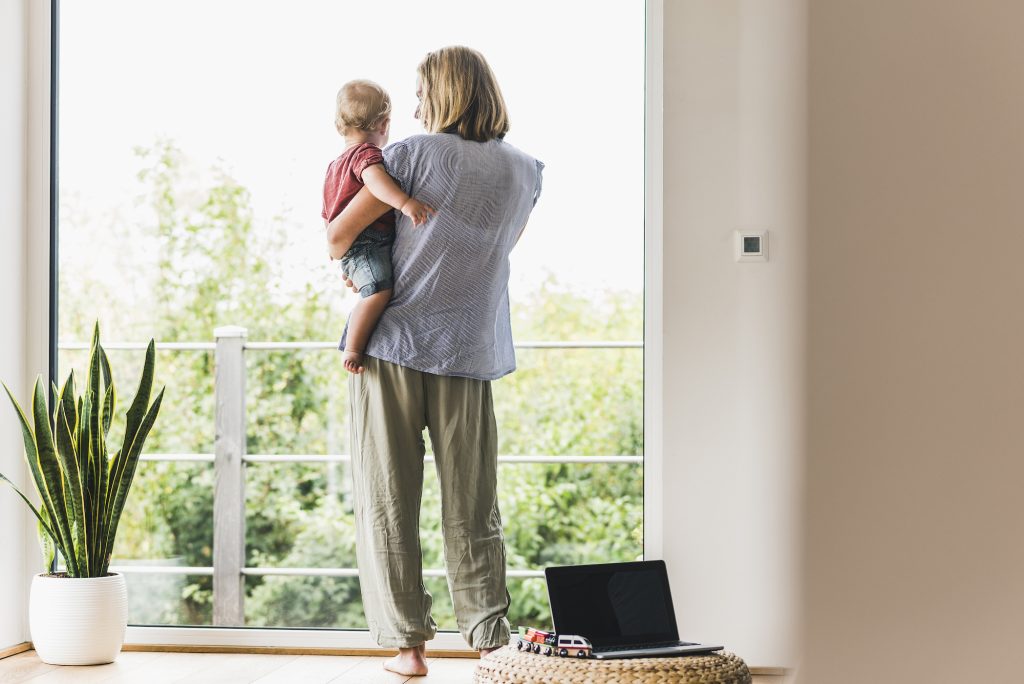 woman holding child looking out large window in modern home