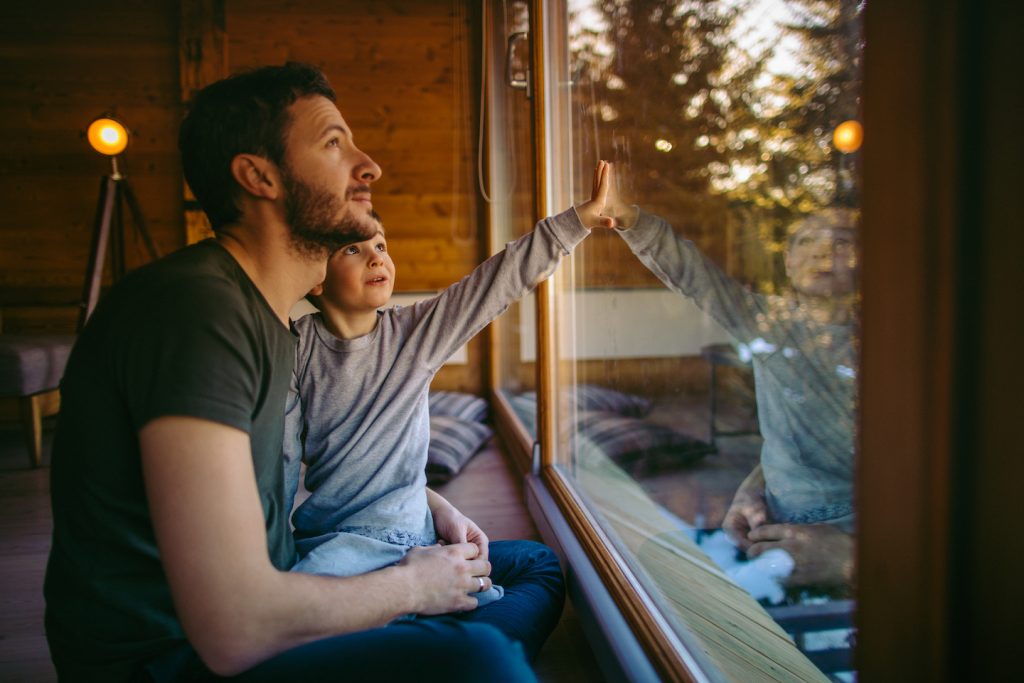 Father and young son look out glass window