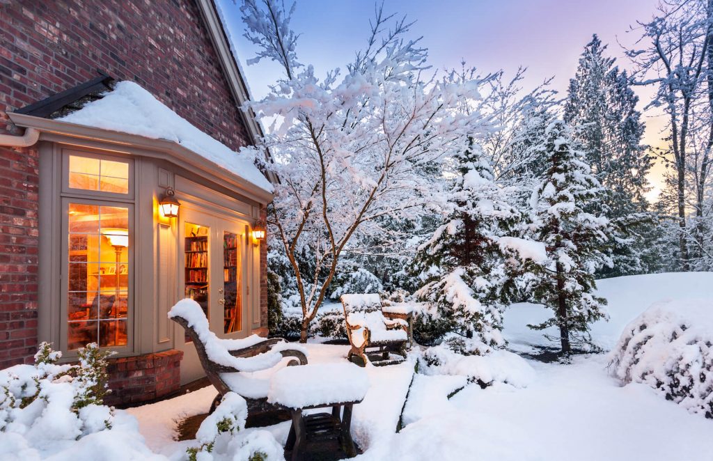 an outdoor snowy house scene with a warmly lit window reminds us of higher heating prices ahead 