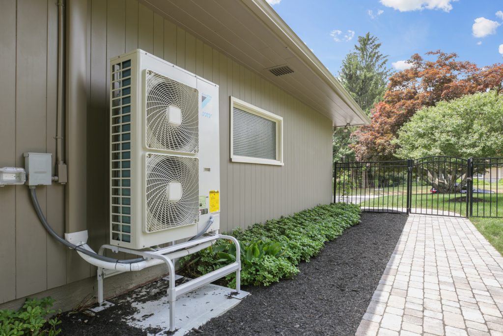 heat pump condenser outdoors on exterior wall of grey house