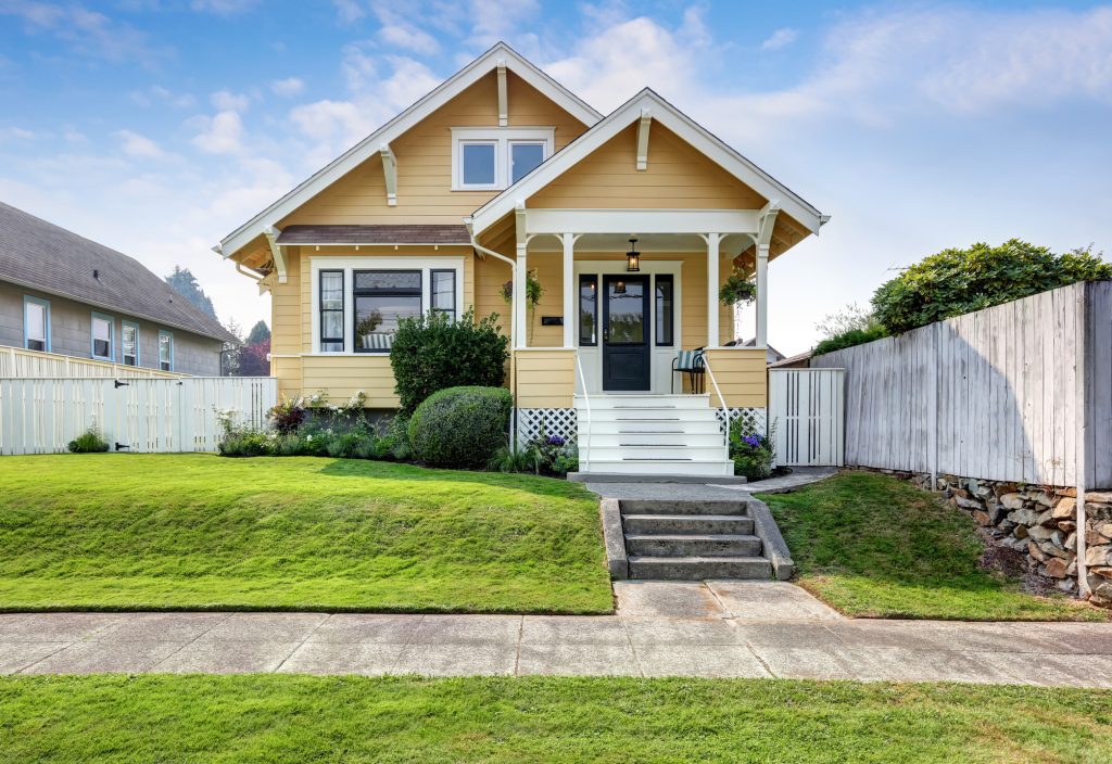 exterior of modest craftsman home with yellow siding and tidy yard with green grass