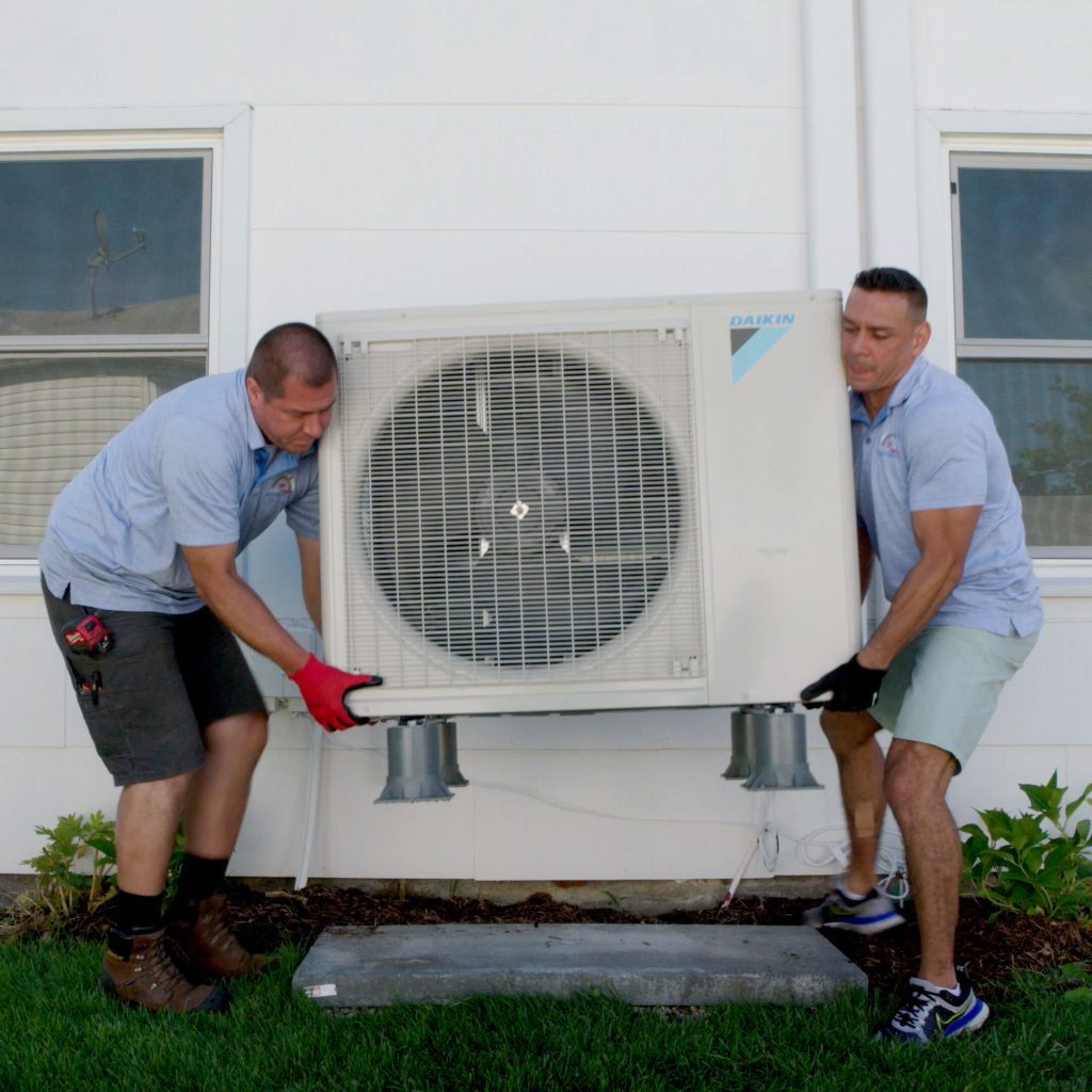 two professionals working together fro heat pump installation of condenser outside house