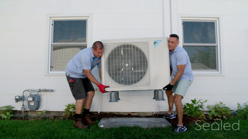 two HVAC professionals install a heat pump outdoor compressor unit