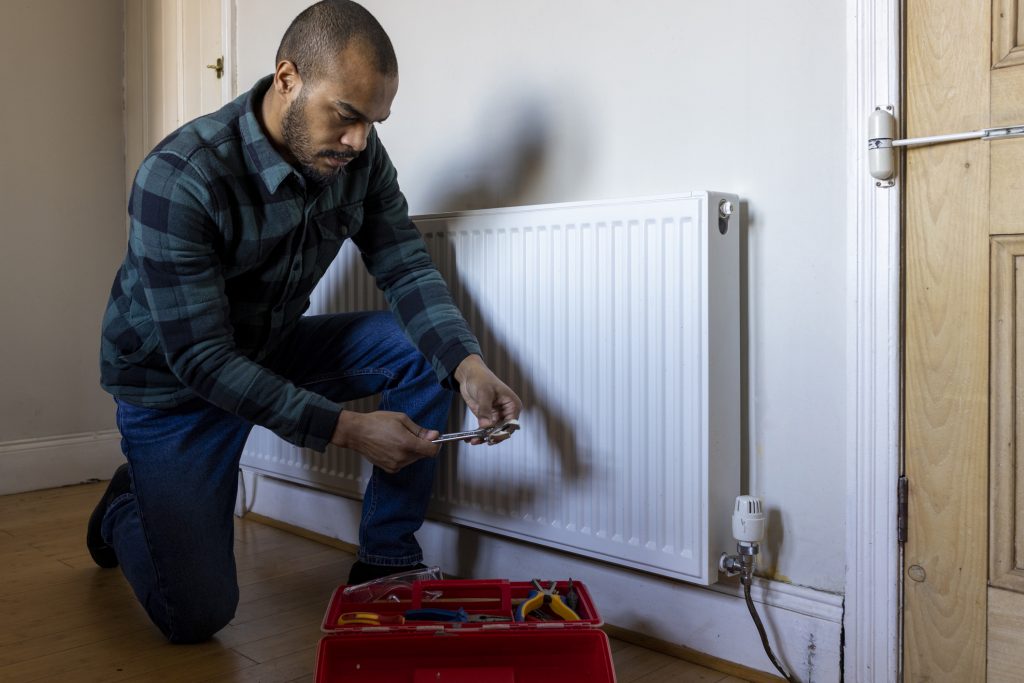 man maintaining an older radiator that isn't working in home