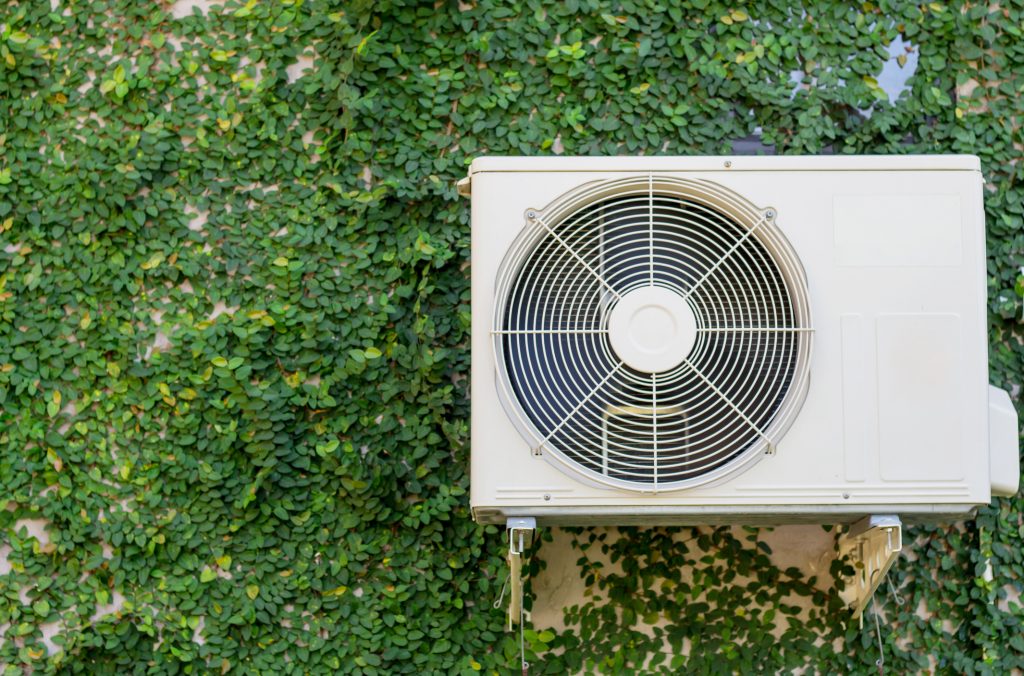 heat pump outdoor compressor unit on green ivy wall: should you choose a geothermal or air source heat pump?