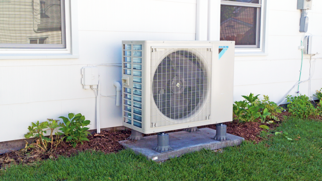outdoor heat pump condenser unit against white house exterior