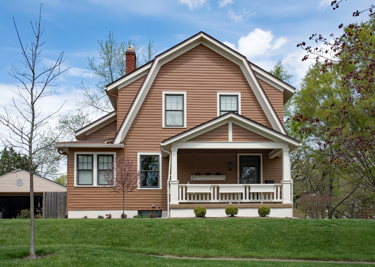 Front exterior of an adorable brown dutch colonial home with full front porch and green yard