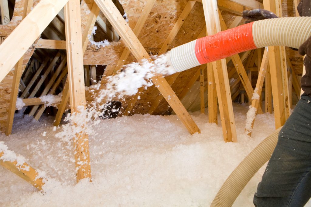 worker spraying cellulose insulation into attic with hose to reduce energy waste and increase comfort