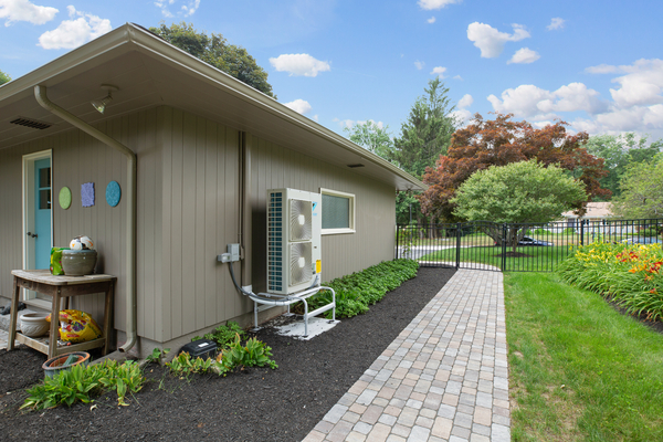 A heat pump is installed on the exterior of an older home with a well-manicured lawn