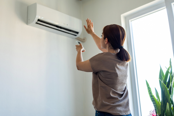 Woman holds her hand to a mini split AC with a remote in a brightly lit home