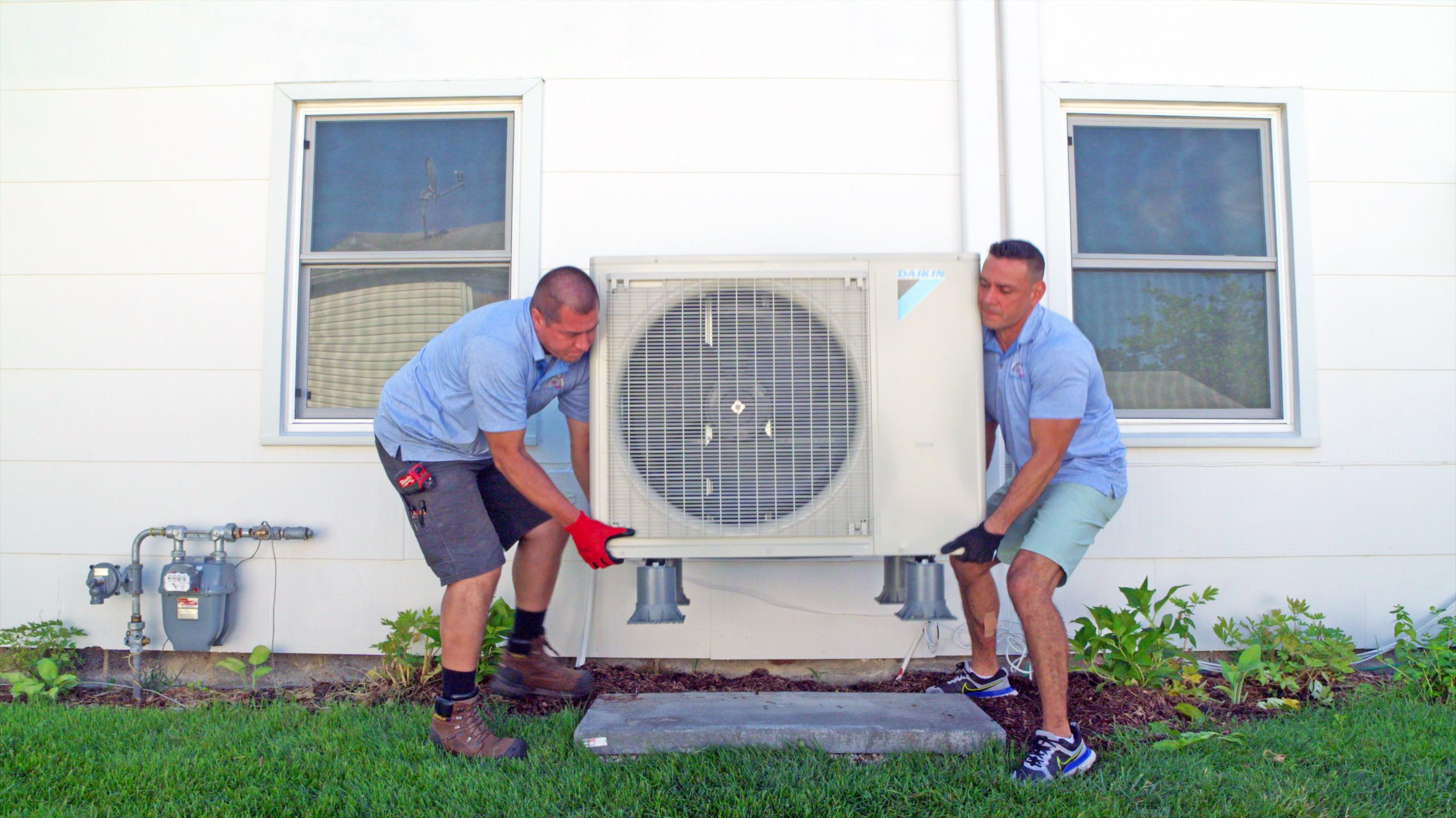 Two HVAC professionals install a heat pump outdoor unit