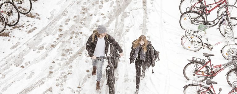 Two students walking with a bike on winter time.