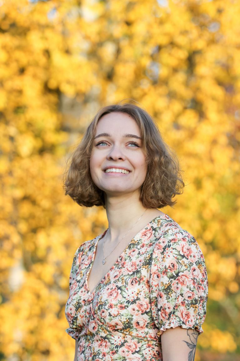 Young woman with curly hair standing in front of yellow leaves