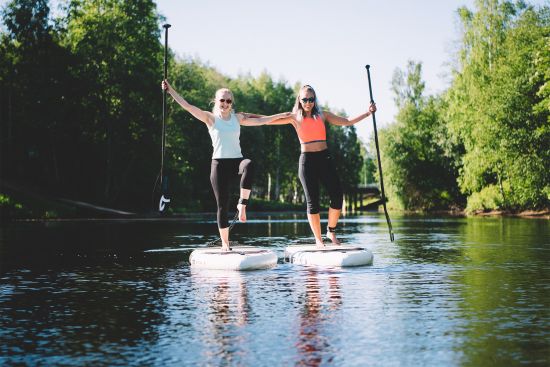 Kaksi nuorta henkilöä sup-lautojen päällä joella./ Two young people on sup-boards on the river. 