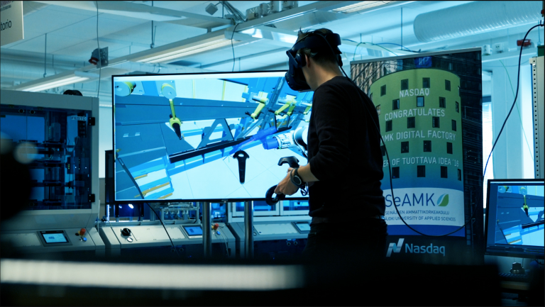 VR-laseja käyttävä henkilö tutkii robottisolu virtuaalitodellisuudessa