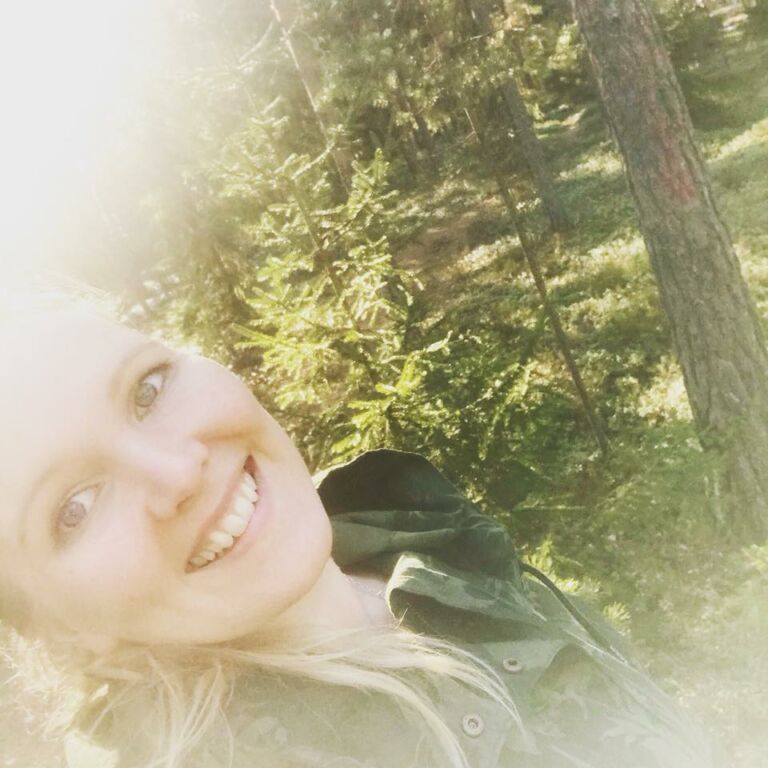 Vaalea nainen hymyilee taustallaan vihreä metsä.