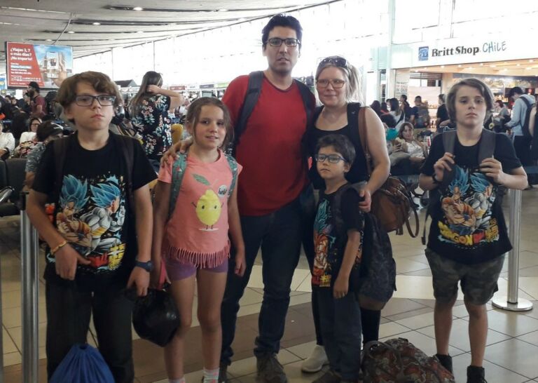 Kaksi aikuista ja neljä lasta seisovat lentokentän odotusaulassa matkatavaroiden kanssa.