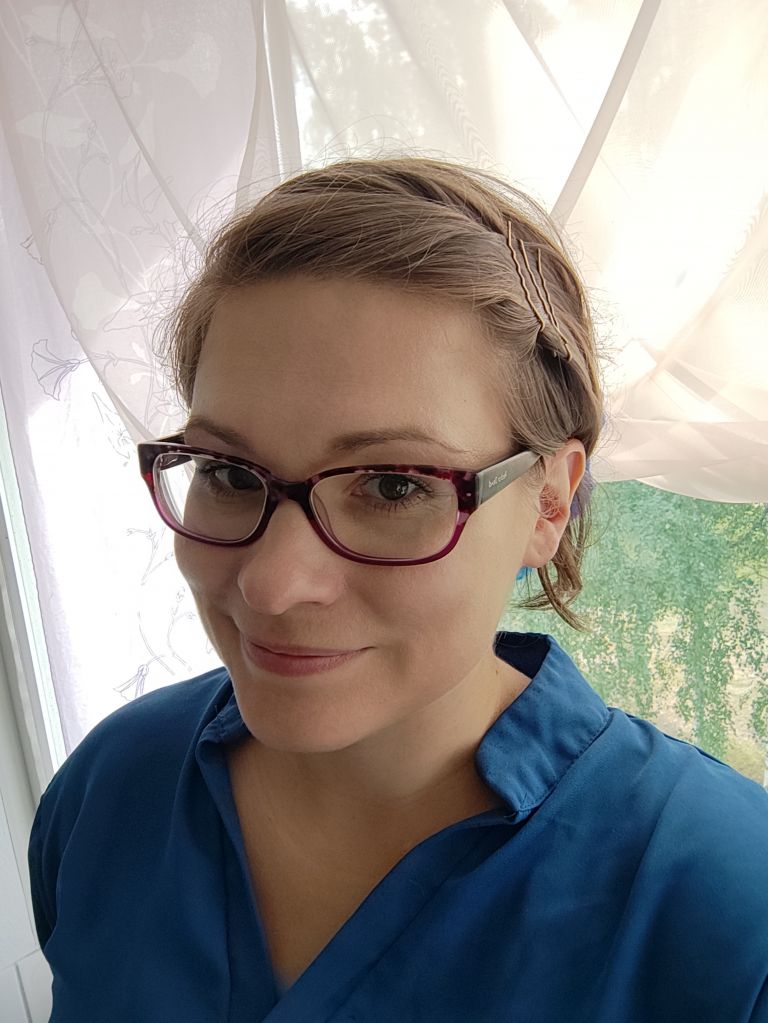 Woman with eye-glasses stands in front of a window.