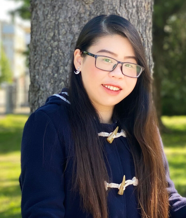 Dark-haired woman sits in front of a tree on a lawn.