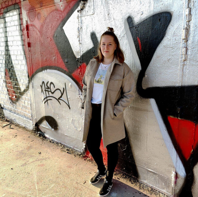 Nuori nainen seisoo seinään tehdyn graffitimaalauksen edessä.