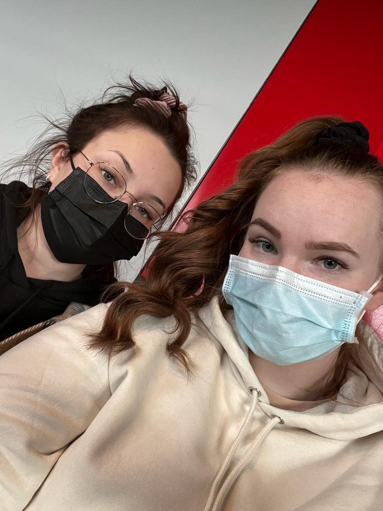 Two dark haired students pose for camera with face masks on.