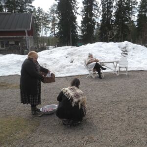 Kkai henkilö pesee käsipyykkiä ja yksi istuu tuolissa.