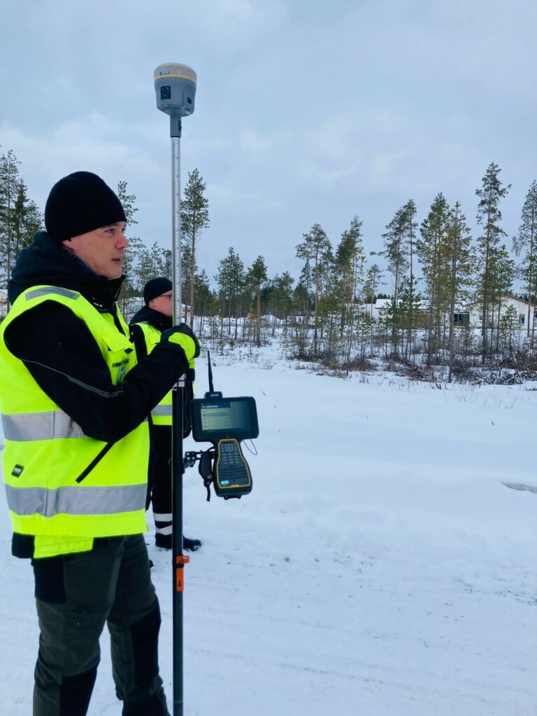 Mies pitelee GNSS-paikanninta lumisessa maastossa.