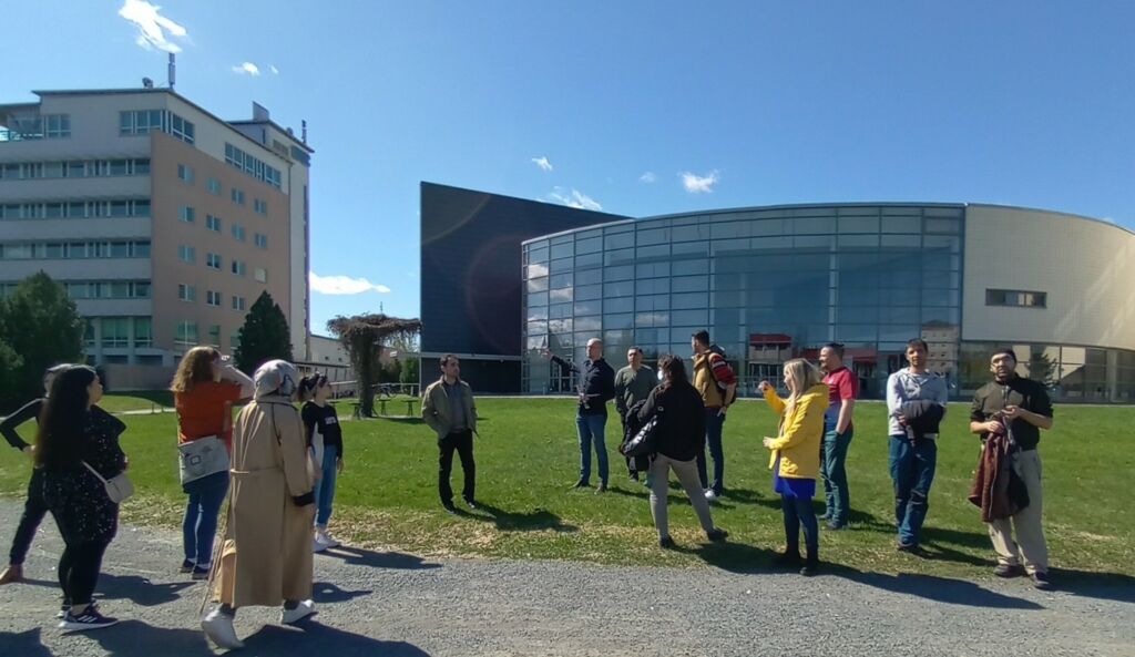 Ihmisiä ulkona nurmikolla rakennuksen edustalla.