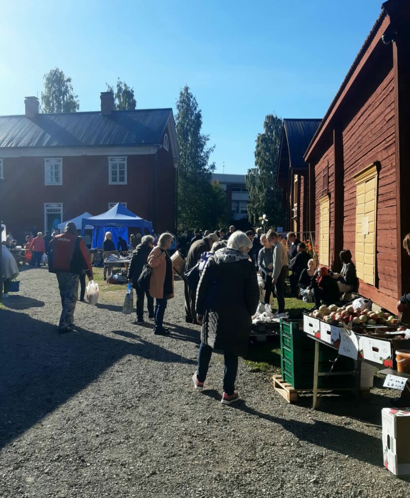 Ihmisiä tutustumassa tuotteisiin vanhojen pohjalaistalojen pihamaalla.