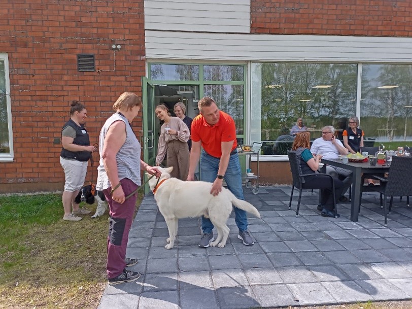 Ihmisiä ja koiria punatiilisen rakennuksen edustalla.