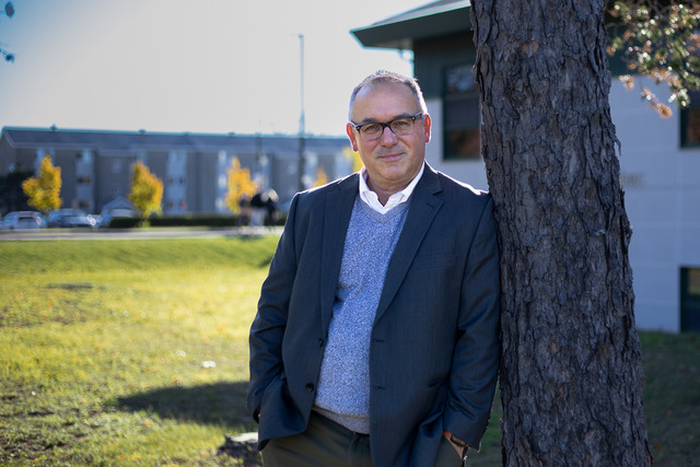 A man in smart casual otufit standinga and leaning on a tree.