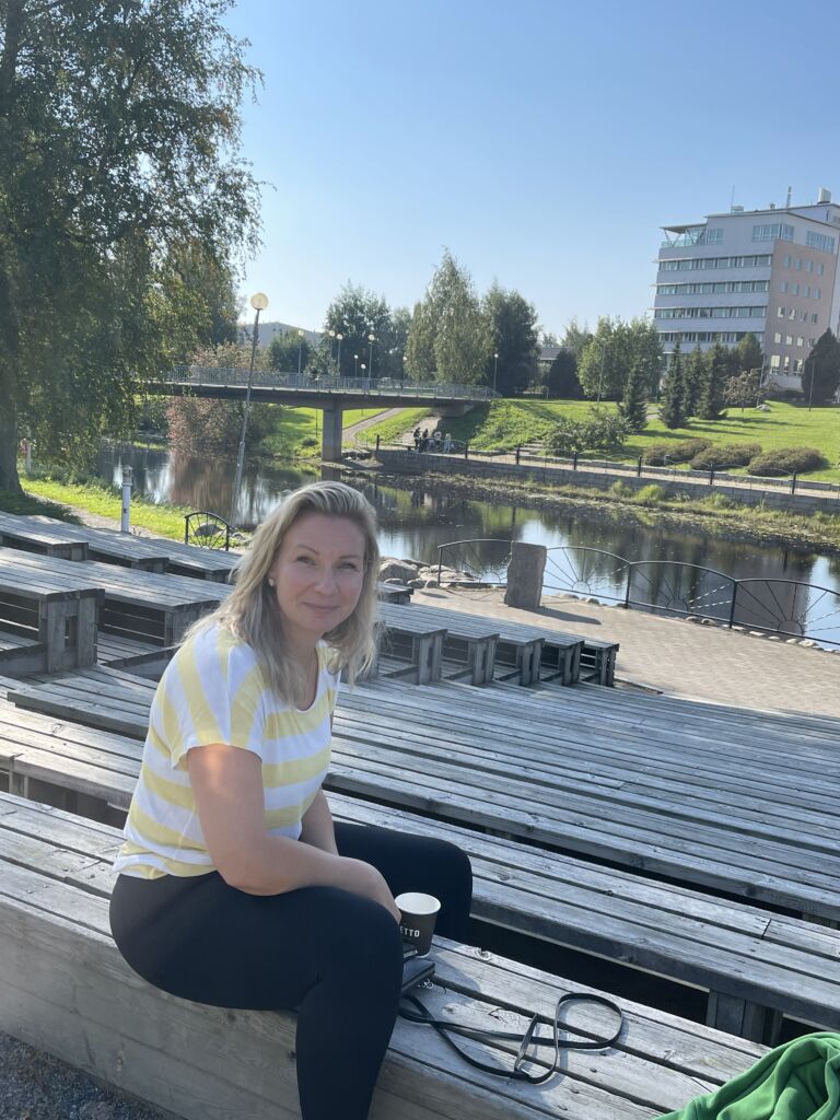 A person sitting on the campus beach in the amphitheater. The campus and the river can be seen in the background.