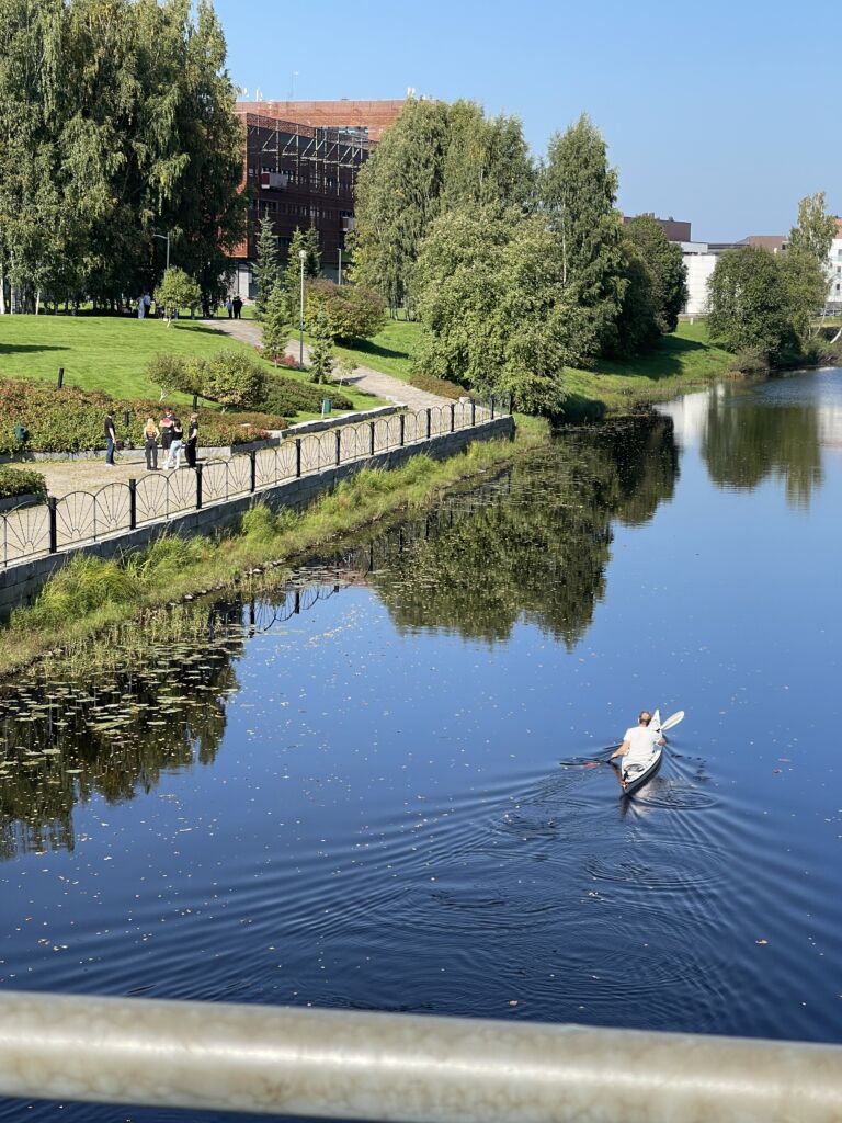 A river where a person is paddling. The Frami F building is visible in the background.