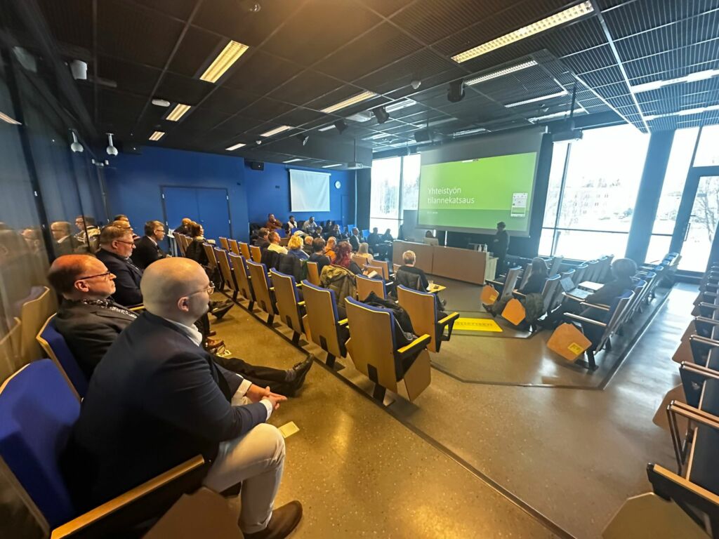 Ihmisiä auditoriossa seuraamassa esitystä valkokankaalta.